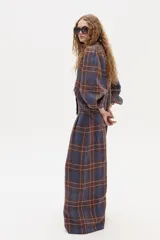 Camisa de lino a cuadros azules y marrones, con cuello camisero clásico, mangas largas abullonadas con puños ajustados con terminación de onditas, botones de nácar frontales y ruedo curvo, un poco más largo atrás.