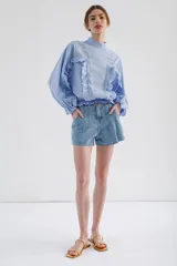 Blusa lila de cuello alto y manga 3/4 con elástico en el bajo. Presenta volados verticales en el frente.