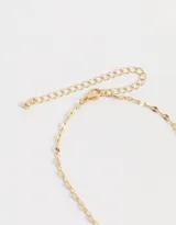Collar largo dorado con cadena de eslabones planos y dijes colgantes: corazón con borde dorado y centro iridiscente, corazón dorado con strass y cuarzo rosa facetado.