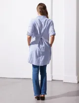 Camisola larga de algodón color blanco, marca Dash. Tiene cuello con solapa, abertura central con botones, bolsillo aplicado en el pecho, mangas regulables con presilla y botón, y bolsillos laterales en la costura.
