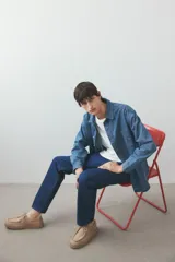 Camisa de denim azul de algodón rígido, corte holgado, cuello inglés, tapeta clásica con botones blancos, bolsillo de parche en el pecho, canesú en la espalda, mangas largas con puños abotonados y bajo levemente redondeado.