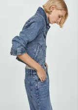 Chaqueta de jean azul de corte clásico, con cuello camisero, mangas 3/4 con puños arremangados, cierre frontal con botones metálicos, bolsillos de parche con solapa abotonada en el pecho y bolsillos laterales.