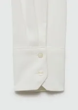 Camisa blanca de tejido fluido, corte recto, manga larga con puños abotonados, cuello camisero y cierre frontal con botones.