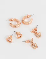 Set de tres pares de aros bañados en oro rosa: aros pasantes con forma de corazón, aros colgantes con forma de mariposa con strass y aros tipo argolla con textura. Todos con cierre a presión.