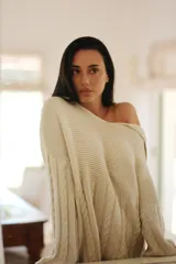 Buzo de tejido de punto color crudo, con cuello amplio que puede usarse caído sobre los hombros, mangas largas con trenzas de ochos y cuerpo con punto arroz.