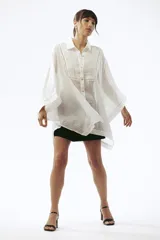 Camisa blanca de lino con corte amplio, cuello clásico, cierre frontal con botones y mangas anchas.