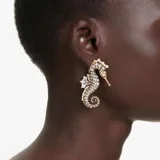 Par de aros colgantes con forma de caballito de mar, con cristales blancos y perlas engarzadas en metal dorado. Cierre de clip.