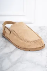 Zueco color beige de gamuza, con plantilla de corcho, detalle de costuras en la parte delantera y tira trasera ajustable con hebilla.