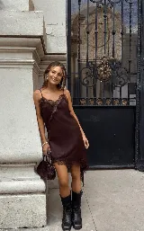 Vestido lencero (slip dress) color marrón oscuro, con tirantes finos y detalles de encaje en el escote y el ruedo asimétrico.