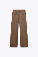 Pantalón de jean color marrón, de tiro alto, corte wide leg y relaxed fit. Cuenta con bolsillos delanteros y traseros, trabillas en la cintura, cierre frontal con cremallera, botón interior y gancho metálico.