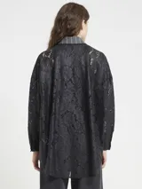 Camisa de manga larga con rayas verticales grises y blancas, cuello camisero y cierre frontal de botones oscuros. Las mangas son de encaje negro, y el frente presenta una aplicación decorativa de lentejuelas y cuentas negras en forma de flor o estrella.