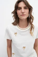 Remera blanca con bordados de palmeras, de corte clásico y manga corta.