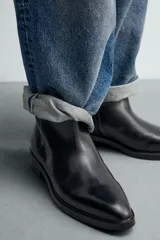 Bota de piel negra con punta fina, cierre de cremallera lateral y tacón bajo.