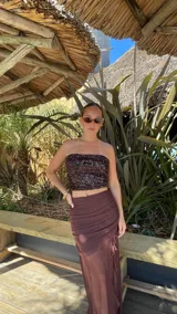 Pollera larga de microtul color marrón, con diseño de transparencias, detalle de fruncido lateral y volados verticales a lo largo de la abertura frontal.