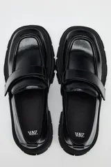 Zapato tipo mocasín negro con plataforma y suela track. Presenta tira ajustable adherente y tirador trasero.