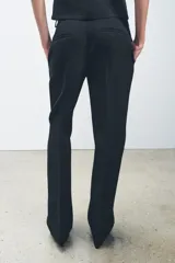 Pantalón negro de tiro medio con cintura con trabillas y corte flare. Cierre frontal con cremallera, botón y gancho metálico.