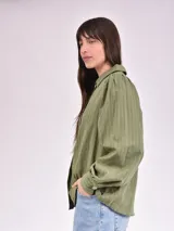 Camisa verde con rayas verticales, cuello clásico, cierre con botones y mangas largas abullonadas.