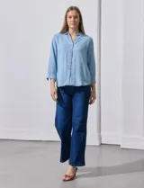 Camisa celeste de tencel con cuello con solapa, escote en V, abertura central con botones y mangas 3/4 regulables con presilla y botón.