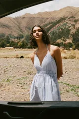 Vestido midi a rayas verticales azules y blancas, con escote en V, tirantes finos y cintura elástica. Presenta bordados florales calados en el ruedo.