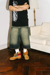 Bermuda baggy de jean con lavado verde, bordado en negro y rojo, cierre y botón personalizado, corte amplio y bolsillos grandes.