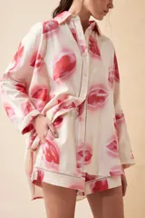 Camisa oversize de lino con estampado de labios en tonos rosados y rojos. Tiene cuello clásico, cierre frontal con botones y mangas largas. Detalles de calado en los bordes. Completa el conjunto con el Short Lipstick.