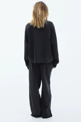 Pantalón deportivo negro de corte holgado, con cintura elástica y cordón ajustable. Confeccionado en felpa de algodón liviano con efecto lavado, bolsillos laterales y bajos sin rematar.