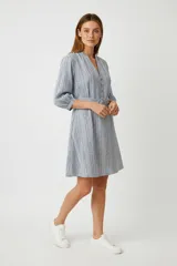 Vestido corto de algodón con estampado de rayas verticales finas en tonos azules y blancos. Presenta cuello profundo en V con botones frontales y mangas tres cuartos. Incluye un lazo para ajustar a la cintura.