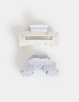 Set de dos broches para el pelo, uno tipo clip rectangular color crema con estampado de flores y cuadros celestes, y otro tipo clip con forma de arco con corazones y estampado de cuadros rosas y celestes.