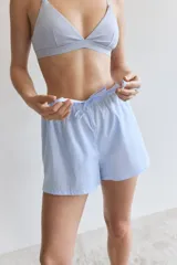 Shorts de pijama celestes con cintura elástica y cordón ajustable. Uno de los lados es de tela a rayas verticales blancas y celestes.