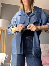 Camisa de denim fino color azul con cuello clásico, cierre frontal con botones y mangas largas con puños abotonados.