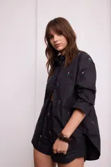 Camisa negra con bordado de flores rosas, corte recto, cuello clásico y cierre frontal con botones.