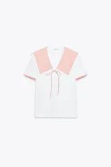 Camiseta blanca de cuello bobo con terminaciones bordadas y detalle de lazo en el delantero. El cuello y las mangas cortas son de tela a cuadros vichy color salmón.