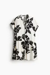 Vestido corto tipo túnica color blanco con estampado de flores negras, cuello mao, mangas cortas con doblez, botones frontales y falda con vuelo. Corte holgado.