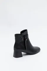 Bota corta de caña baja color negro, con puntera cuadrada, taco medio y tira decorativa con hebilla metálica en el lateral.