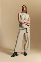 Pantalón de vestir de tiro alto, color beige claro con finas rayas verticales oscuras. Es de corte ancho y largo, con un lazo de tela a juego anudado en la cintura. Se combina con un top sin mangas del mismo tejido y color.