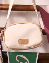 Bandolera de cuerina color crema con contorno marrón y correa de tela color beige. Tiene un tag frontal con el logo "The Brunch Club" y un charm lateral decorativo.