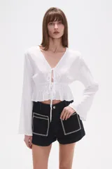 Blusa de rayón color blanco con detalles de broderie, cuello en V y cierre frontal con cordones para atar. Presenta mangas largas y cintura elástica con terminación en volado.