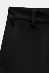 Pantalón negro de tiro alto con trabillas en la cintura, bolsillos delanteros y traseros, raya planchada en el frente, pierna recta y bajo acampanado.