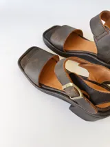 Sandalias de cuero color chocolate, con tira ancha sobre los dedos, pulsera al tobillo con hebilla metálica y taco cuadrado de 6 cm.