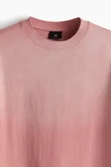 Remera rosa con efecto desteñido, corte amplio, cuello redondo y mangas cortas.