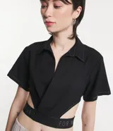Camisa corta negra con cuello camisero, mangas cortas y aberturas laterales con elástico con letras blancas.
