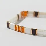 Pulsera elástica con cuentas rectangulares de color blanco, naranja y negro, separadas por cuentas doradas.