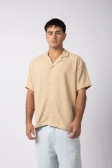 Camisa beige de manga corta confeccionada en lino texturizado, con cuello solapa y cierre frontal abotonado.