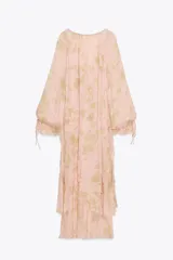 Vestido largo de gasa color rosa pálido con estampado floral en tonos dorados, escote en pico ajustable con lazada, mangas largas abullonadas con elástico y volantes en los puños, forro interior y bajo con volantes escalonados.