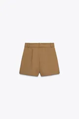 Shorts color marrón confeccionados en hilatura con algodón. Tiro alto y cintura doble con trabillas, bolsillos laterales y falso bolsillo con solapa en delantero. Detalle de costuras a contraste y cierre frontal con cremallera y ganchos metálicos.