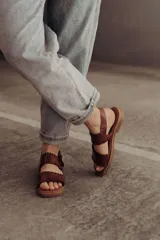 Sandalias de cuero marrón con tiras tejidas a mano y costuras a la vista, con base plana.