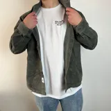 Sobrecamisa color crema de pana con cuello clásico, cierre frontal con botones negros, dos bolsillos de parche en el pecho con solapa abotonada y puños abotonados.