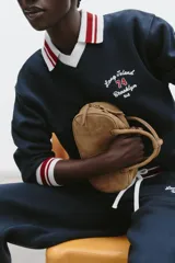 Bolso mini bowling color camel de serraje, con doble asa de mano y correa bandolera extraíble. Tiene un bolsillo interior con cremallera y cierre principal con cremallera y tirador.