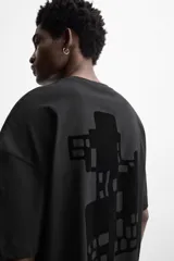 Camiseta negra de corte holgado, cuello redondo y manga corta. Estampado frontal con texto vertical y diseño geométrico abstracto en negro.