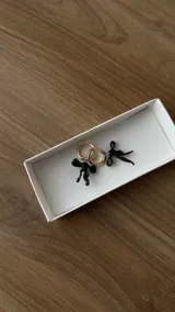 Par de aros colgantes con argollas de acero inoxidable y dijes de vidrio soplado con forma de moño, disponibles en color celeste y rosa.